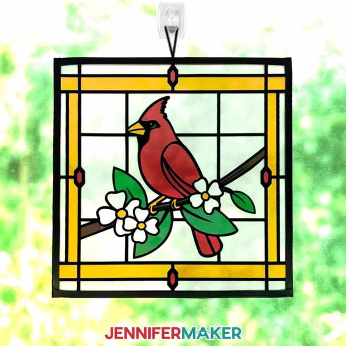Make Stained Glass Using Paper! A paper, acetate, and vinyl stained glass window-inspired project of a cardinal on a branch of white flowers hangs in a sunny window