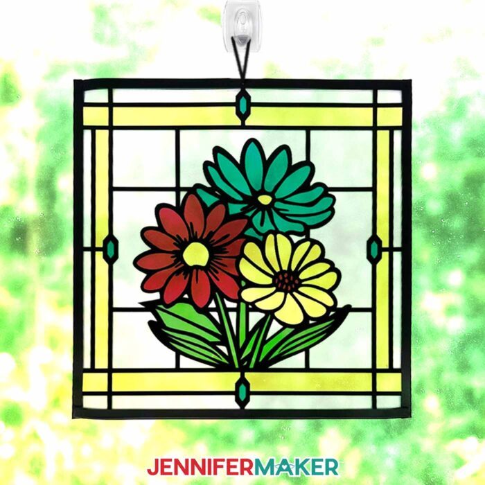 Make Stained Glass Using Paper! A paper, acetate, and vinyl stained glass window-inspired craft depicting a bouquet of flowers hangs in a sunny window