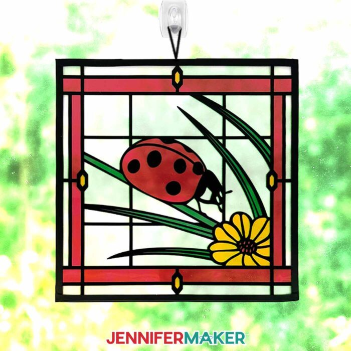Make Stained Glass Using Paper! A paper, acetate, and vinyl stained glass window-inspired craft of a ladybug hangs in a sunny window