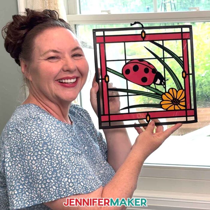 Make Stained Glass Using Paper! Jennifer Maker holds up a stained glass craft of a ladybug in front of a sunny window