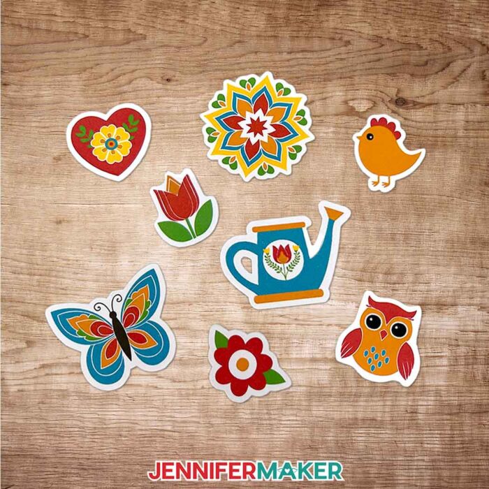 Jennifer Maker's Summer Sticker Starter Pack: 8 of her die-cut stickers spread on a table: blue butterfly, red tulip, red flower, red heart with yellow flower, colorful mandala, orange chick, blue watering can, and red and orange owl.