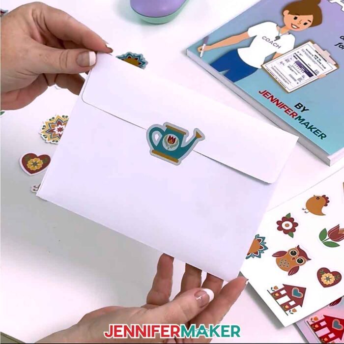 A watering can sticker on a holographic background is used to seal the back flap of a white envelope.