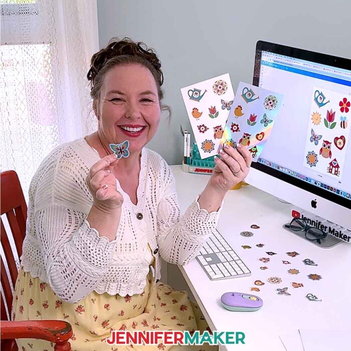 Jennifer Maker sits at her computer desk holding up two sheets of stickers made in Canva plus a die-cut butterfly sticker.