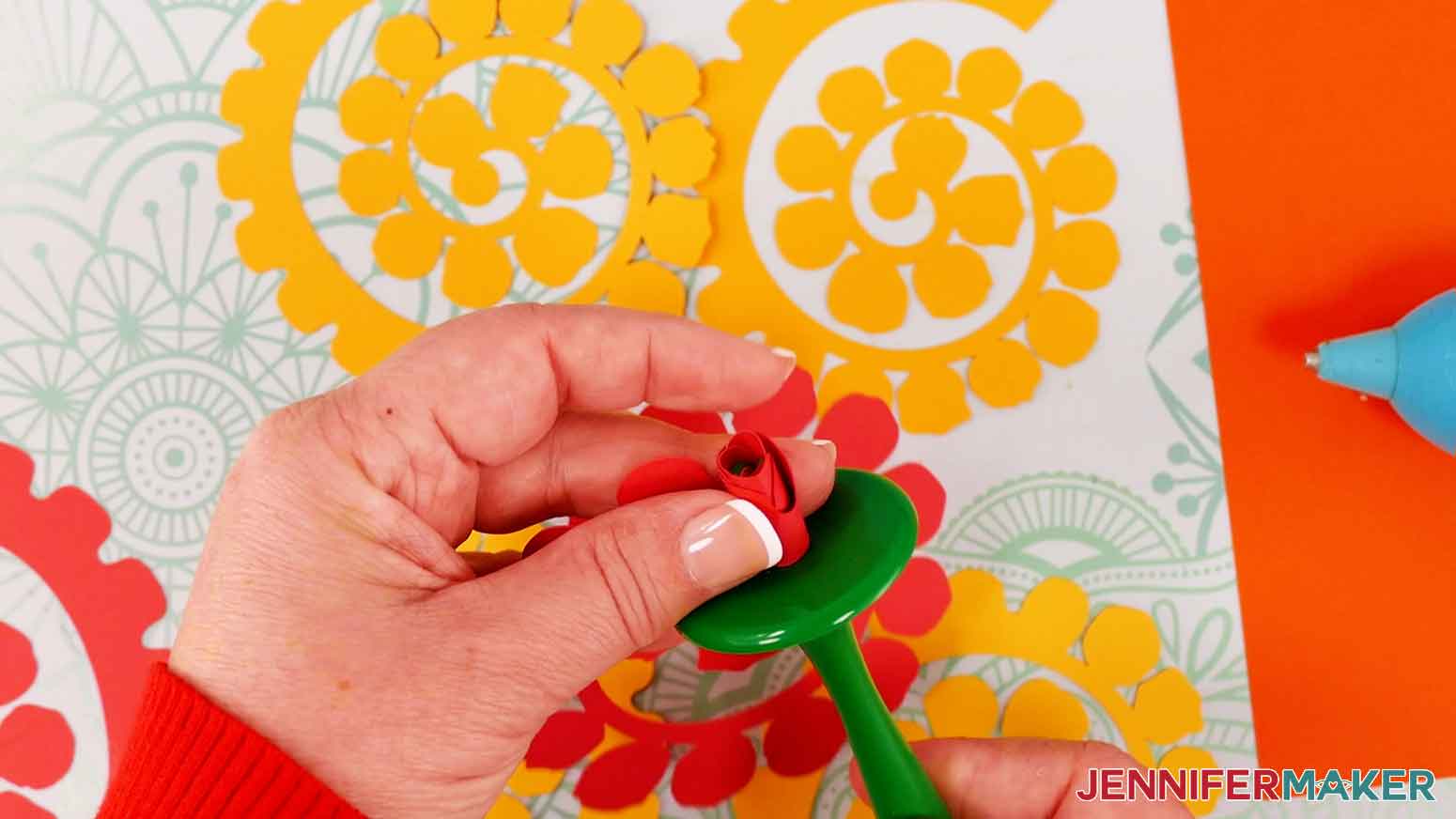 Jennifer is using the Flowtool to roll red, orange, and yellow paper roses.