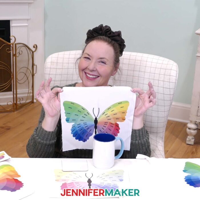 Jennifer sits at her craft desking holding up a sublimated version of her Sublifly color wheel labeled with hex color codes.