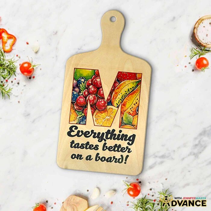 A custom monogrammed charcuterie board with the letter M filled with with fruit and the words "Everything tastes better on a board!"
