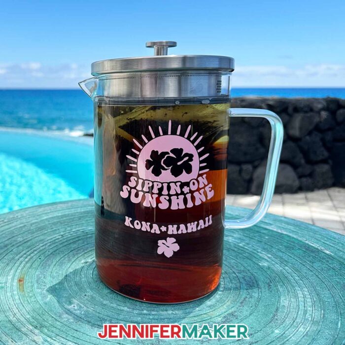 A glass jar of sun tea with a light pink vinyl design that says Sippin on Sunshine, Kona, Hawaii, from a JenniferMaker tutorial.