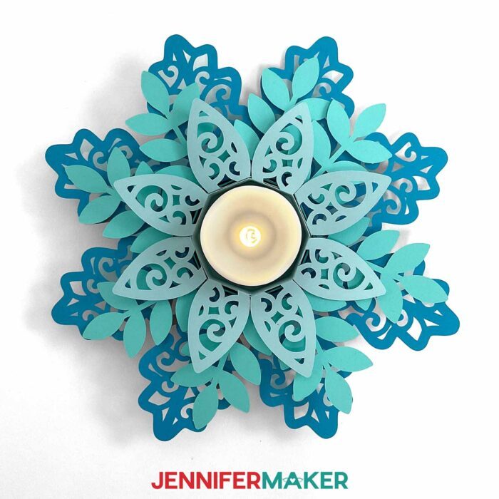 Intricately cut cardstock Tea Light Holder in the shape of a snowflake, made from three shades of blue paper and filled with a glowing LED tea light