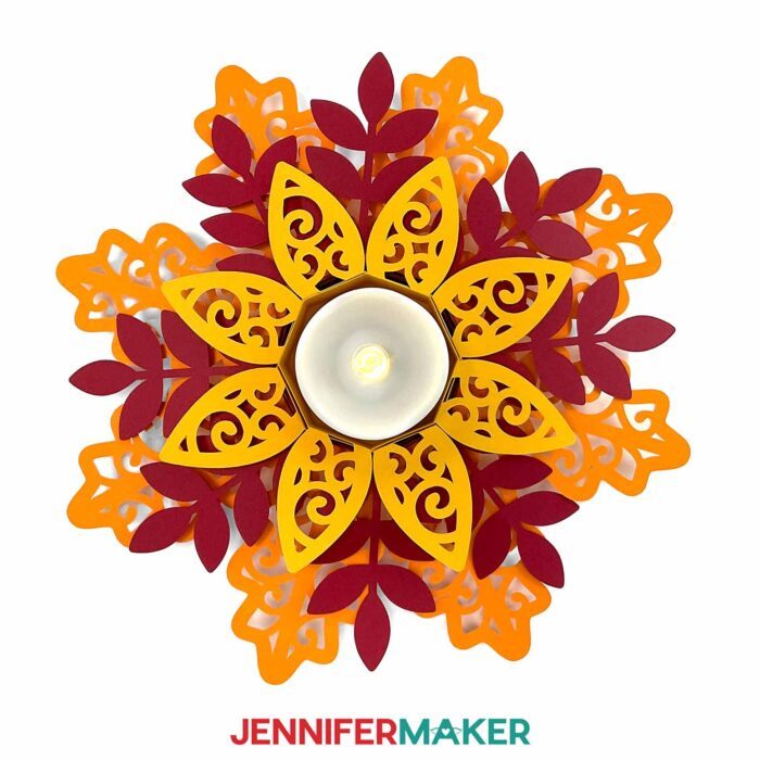 Intricately cut cardstock Tea Light Holder inspired by fall leaves, made from shades of orange and red paper and filled with a glowing LED tea light