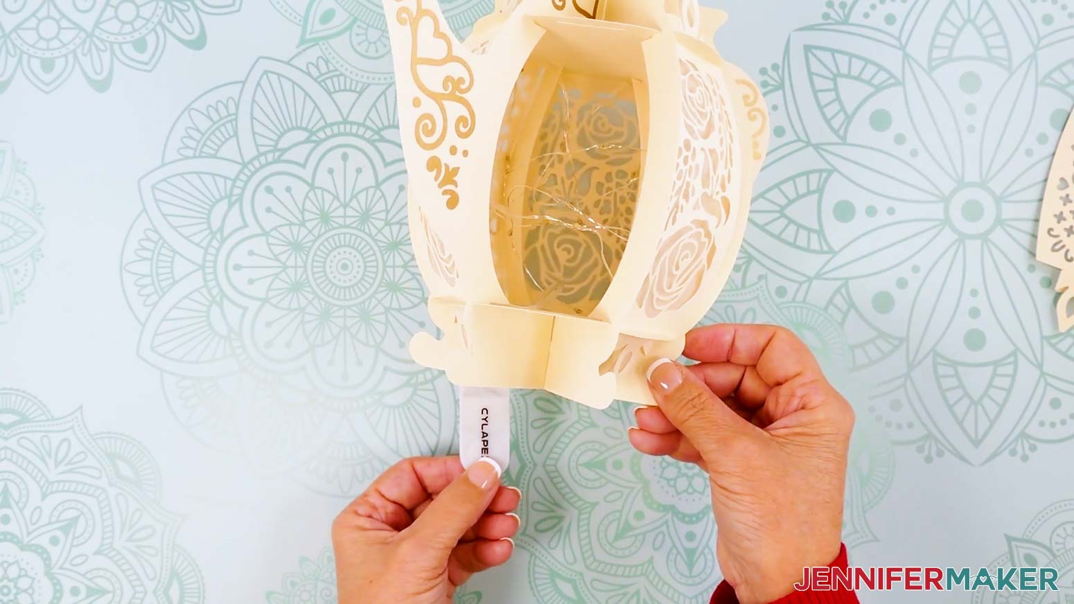 A coil of fairy lights being inserted through the open teapot lantern panel, with the battery pack hanging out a bottom opening.