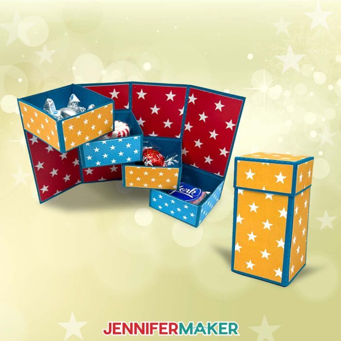 Learn how to make a Tower Gift Box organizer with JenniferMaker! A closed tower gift box with a lid stands on a yellow backdrop. An open tower reveals four panels, each with a small drawer with candies inside. The drawers stack like stairs. Various colored cardstock with white stars decorate the lid, drawers, and panels.