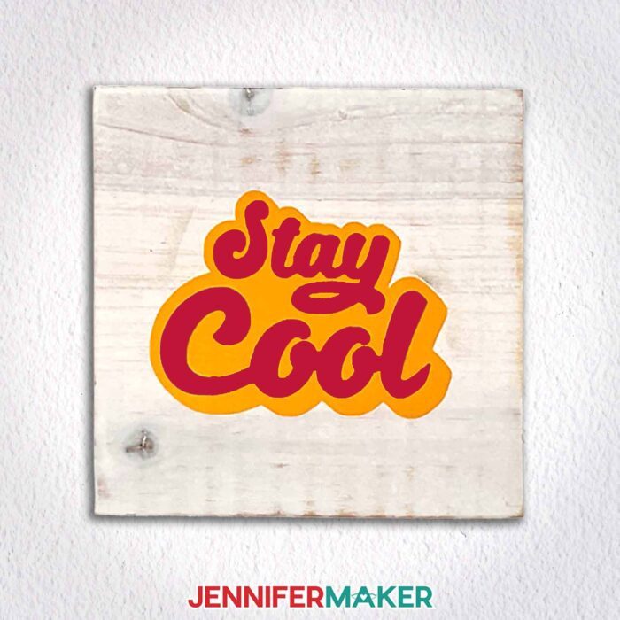 A wooden plaque with "stay cool" in layered red and yellow vinyl hangs on a white wall. Learn how to use transfer tape with vinyl projects with JenniferMaker's new tutorial!