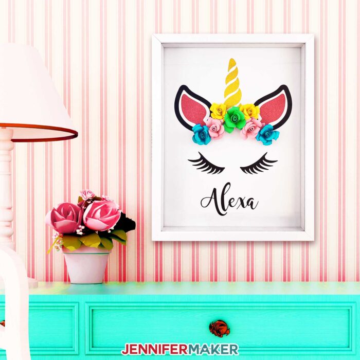 Make a paper flower unicorn shadow box and personalize it with a name using vinyl and cardstock!