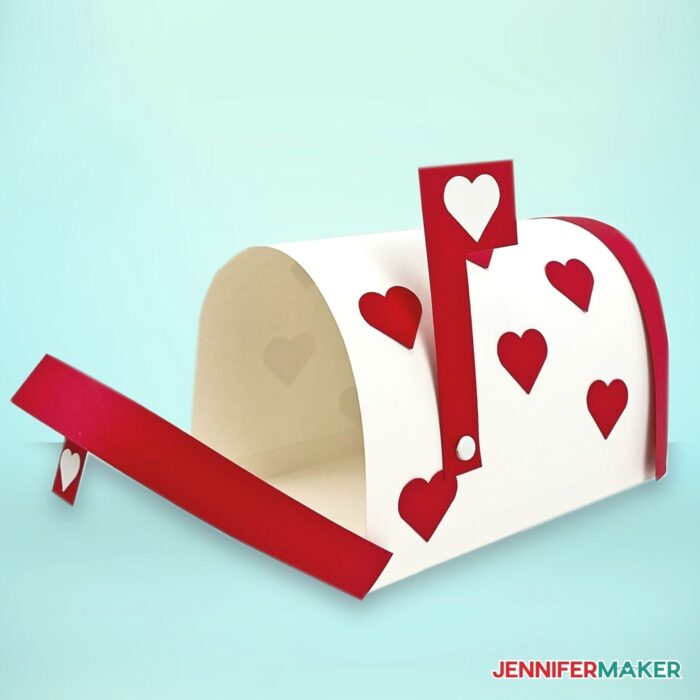 A white Valentine Mailbox Craft made out of paper with red trim, flag, and heart decorations on a light teal background