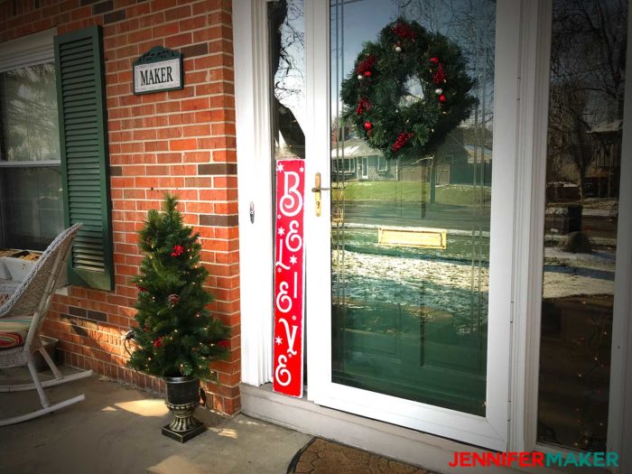 A vertical red "Believe" holiday sign on a front porch for Christmas