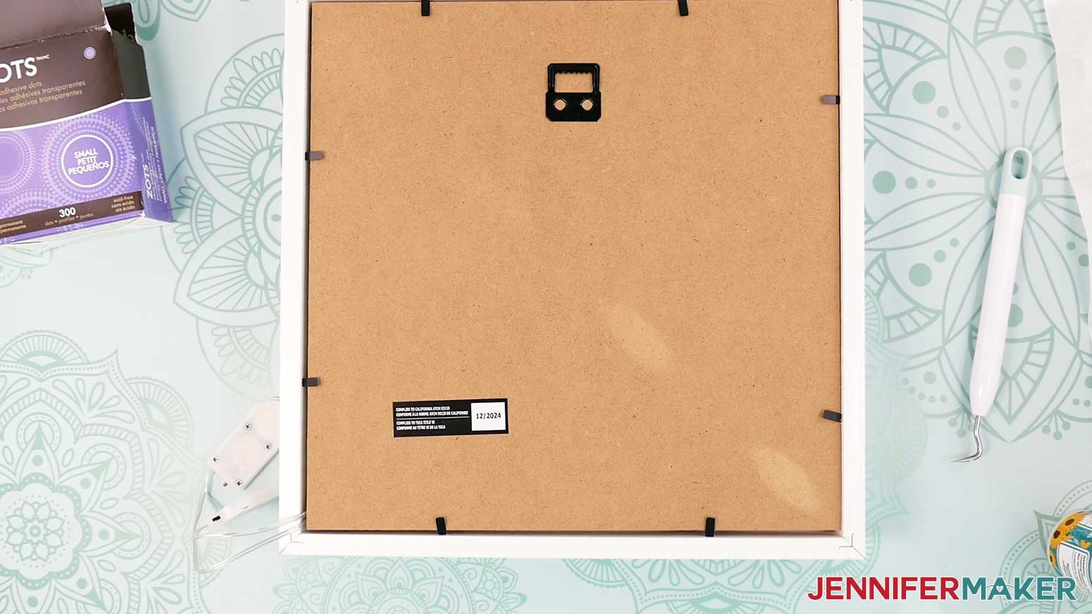 Replace the backer on the frame of the Village Shadow Box With Lights while being sure to keep the light controls outside the bottom corner.