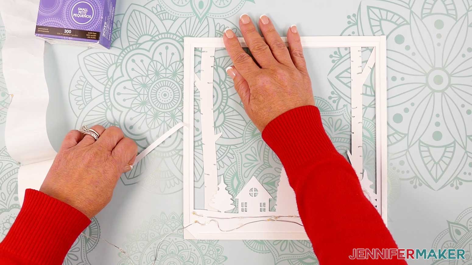 Remove part of the protection cover from the adhesive foam strip on the left side of the second layer of the Village Shadow Box With Lights.