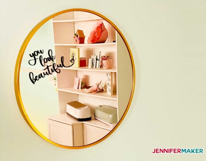 A round gold mirror with the words "you look beautiful" in vinyl in the upper left corner