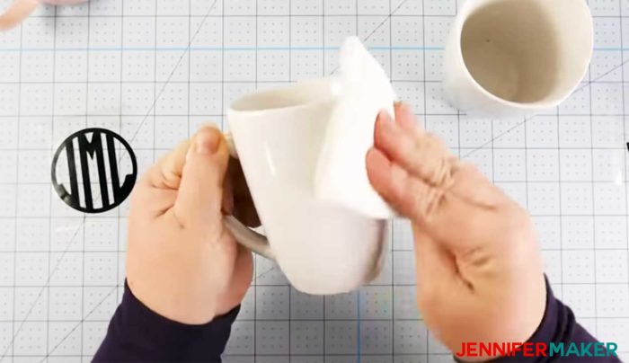 Cleaning a white ceramic mug with rubbing alcohol before applying the vinyl on mug