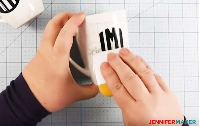 Burnishing black vinyl letters down on a white ceramic mug