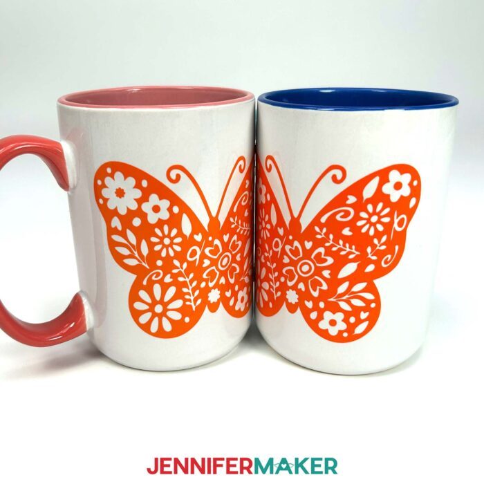 Two white mugs decorated with orange vinyl decals of floral butterflies sit side by side. Learn how to use Adhesive Vinyl Vs Iron-On For Cricut Beginners