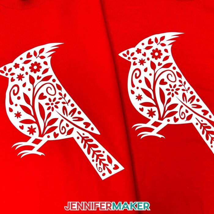 Two red T-shirts with white floral cardinal iron-on vinyl designs sit side by side. Learn how to use Adhesive Vinyl Vs Iron-On For Cricut Beginners