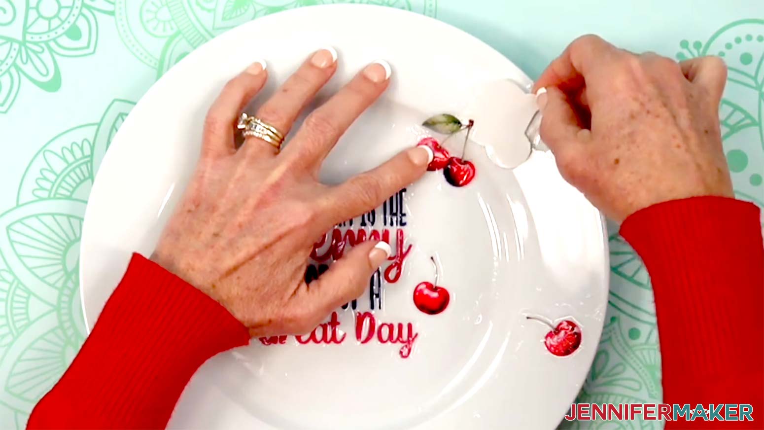 The cherry on the lip of the plate is being held down with the left hand while the right hand slides the backer paper from underneath the cherry waterslide decal.