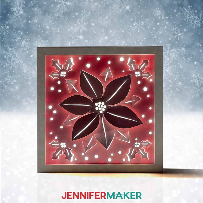 Red Winter Backlit Shadow Box with the image of a poinsettia in the cutouts glows in a snowy scene