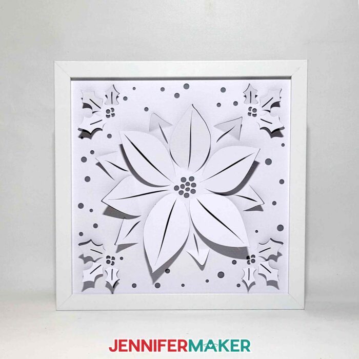 A Winter Backlit Shadow Box with a poinsettia design sits unlit in a white space, calling attention to the detailed cutouts made by a Cricut