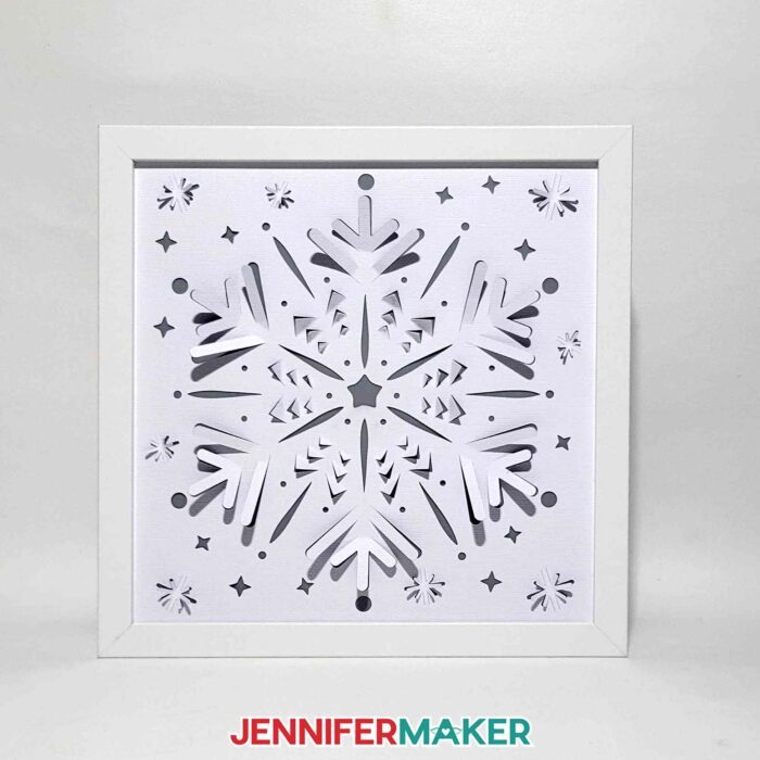 A Winter Backlit Shadow Box in a white frame is shown with the lights off, detailing the intricate cutouts and disguising the hidden vinyl layer