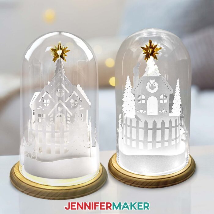 Two glass domes with 3D Cricut cut paper village designs on a table.