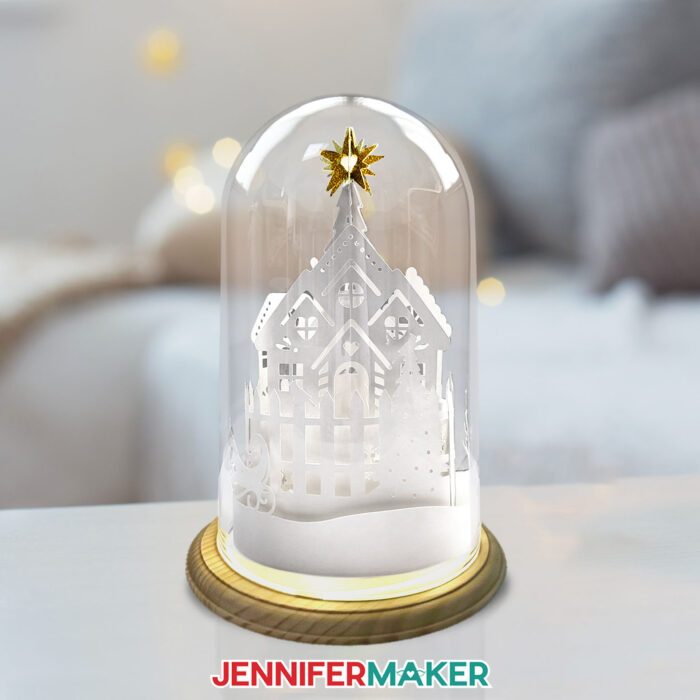 A 3D Cricut cut paper village in a glass dome on a table.