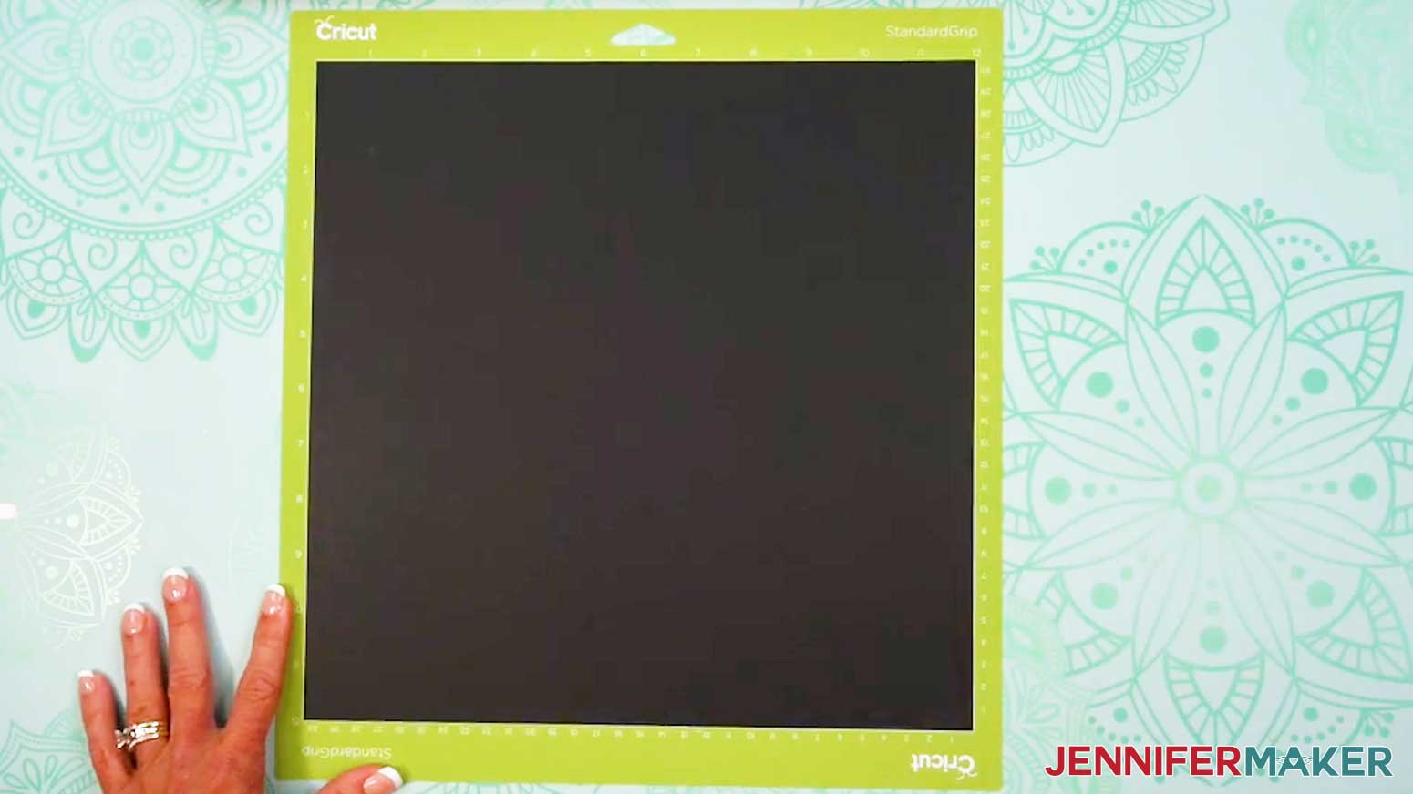 A sheet of 12 by 12 inch black cardstock on a green StandardGrip machine mat.