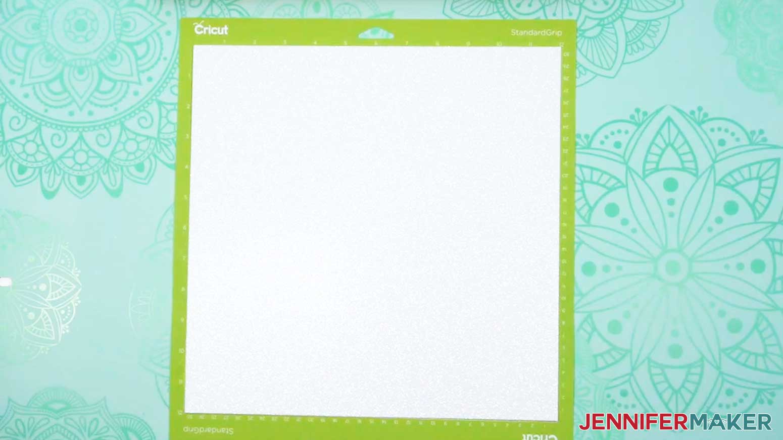 A sheet of 12 by 12 inch white glitter cardstock on a green StandardGrip machine mat.