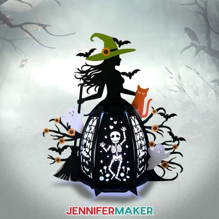 A gorgeous yet spooky Paper Witch Lantern lilluminated against a misty forest background, made of black cardstock with colored details like an orange cat and green witch hat