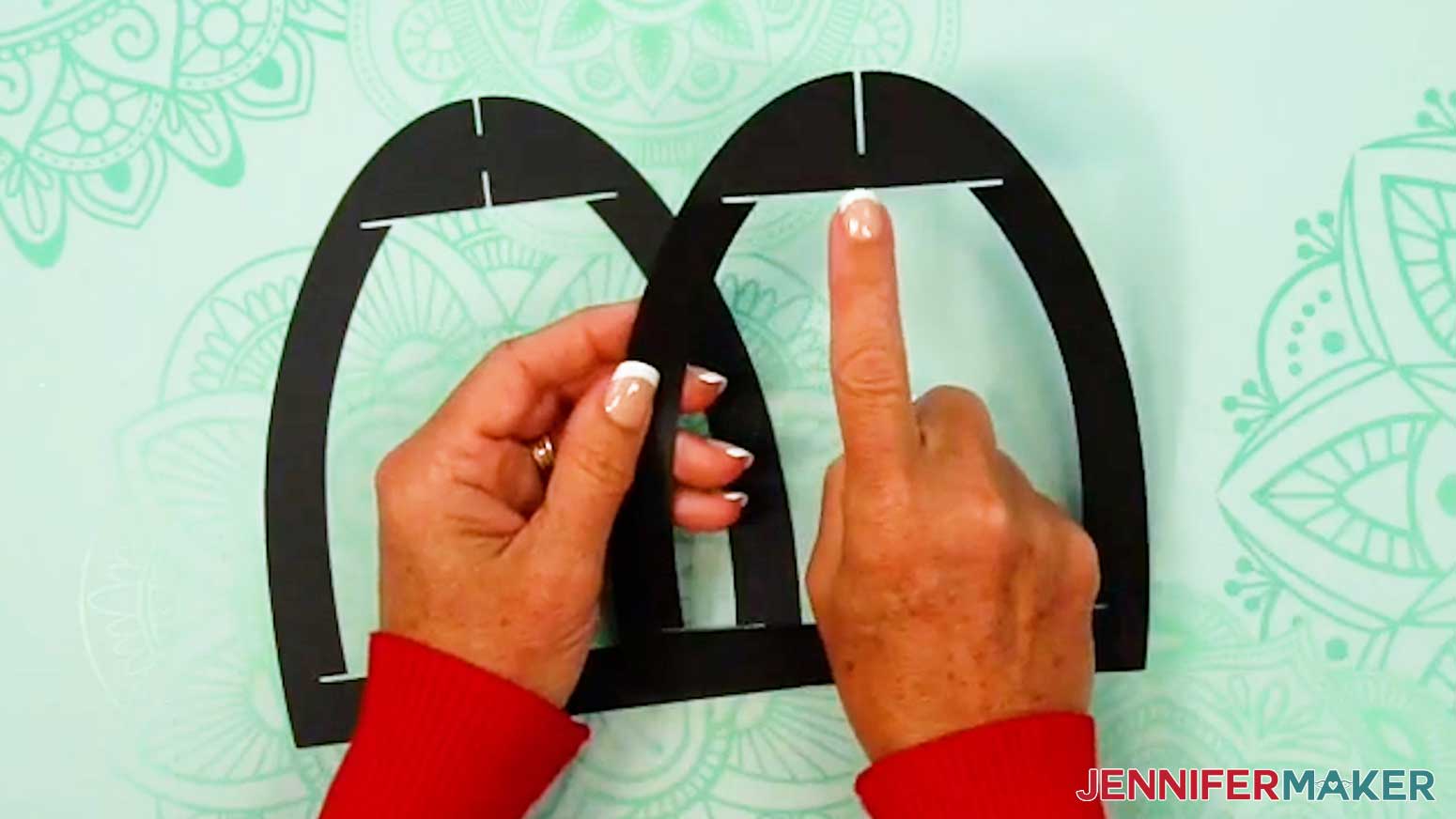 Take the witch lantern frame piece with a slit at the top of the arch and slot it inside the frame piece with slits at the top and bottom of the arch.