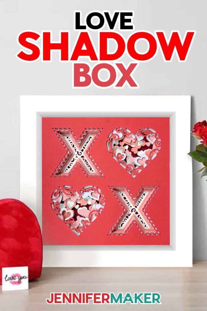 Learn how to make a Northern Lights Shadow Box with JenniferMaker! A cardstock shadow box with a red X and O design with layers of red, pink, and white hearts sits on a table.